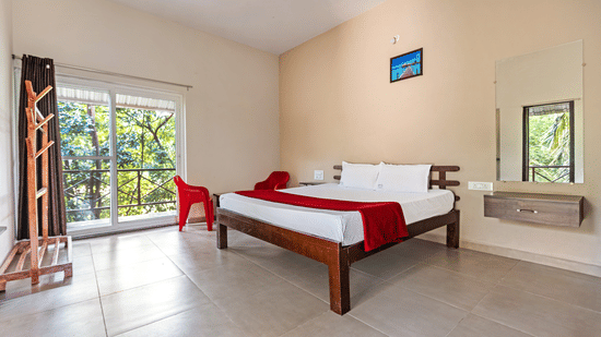 Side view of a clean, minimalist hotel room with tiled floors, a double bed, and natural light from large windows - Nature Trails Ashoka Resort Hampi