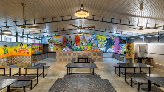 Dining hall with long tables, benches, and a colourful mural on the wall at Nature Trails Durshet.