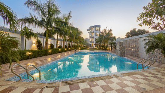 An outdoor swimming pool surrounded by palm trees and a tiled deck during the blue hour at twilight - Nature Trails Rishikesh