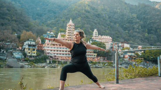 A woman practising the Warrior II yoga pose on a terrace overlooking the River and mountains.