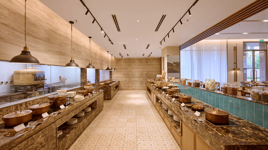 Buffet counters at Flavours in Prachi Sarovar Premiere, Bhubaneswar, arranged parallel to each other with warm stone finishes and under-cabinet illumination.