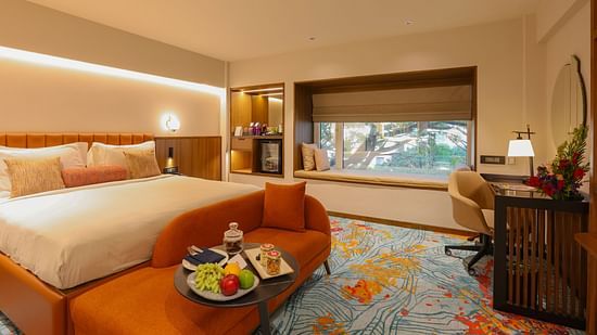 A hotel room with a bed, a couch, and a view of the outside - Pride Hotel Pune