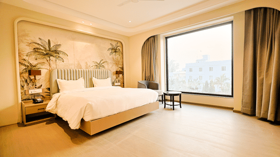 A spacious suite at Pride Premier Alwar featuring a large picture window with a city view, a minimalist headboard design, and an open floor plan.