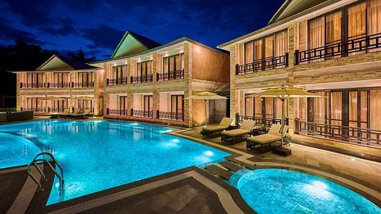 Evening view of hotel pool with glowing blue lights and villa balconies - Royal Tulip, Chitwan