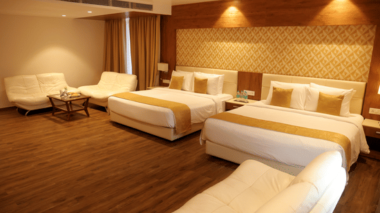 Large room at Sarovar Portico, Somnath with several beds, a seating area, and lighting above the headboard panel.