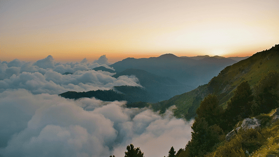 Sunset view from a mountain peak overlooking a sea of clouds and rolling green ridges.