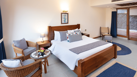 Superior Room at Suryavilas Luxury Resort and Spa featuring a plush bed with a wooden headboard and a lamp on the nightstand next to a seating space for 2 with a coffee table