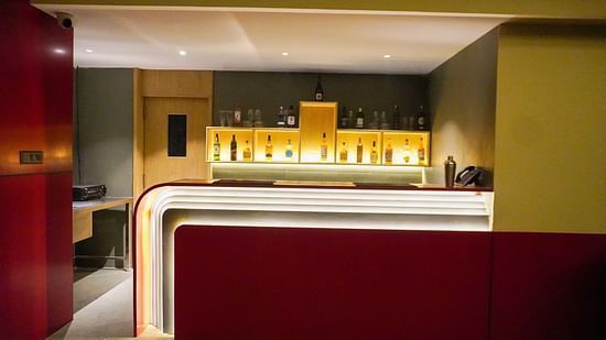 Stylish indoor bar area at Skydip, featuring a sleek white countertop with red accents and warm, inviting backlighting showcasing various bottles - The Orchid Hotel, Chandigarh