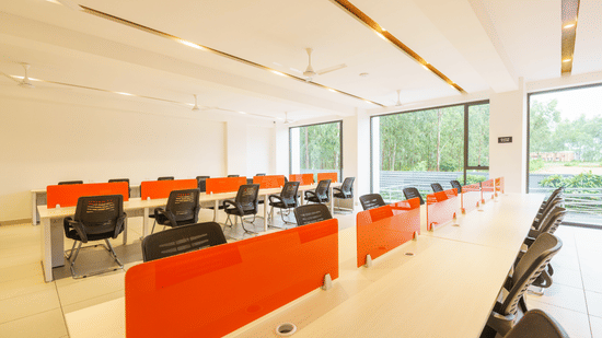 Workstations with black chairs and orange dividers in shared office area near large windows at The Residences at CSE