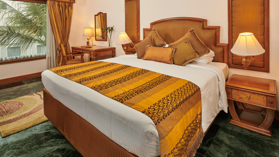The Ummed Ahmedabad hotel room with a comfortable bed, classic wooden furnishings, and warm ambient lighting.