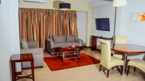 Spacious living area of a suite at The Zehneria, Nairobi featuring sofa seating, air-conditioning, a TV, and a dining table.