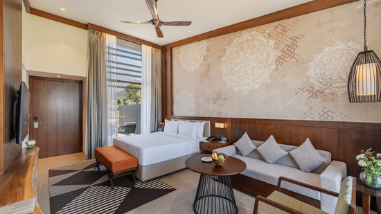 A bedroom in the Villa With Terrace at Vandhara Sarovar Premiere, Patkote, with a sofa, a coffee table with fruit, and decorative wall panels behind the bed.