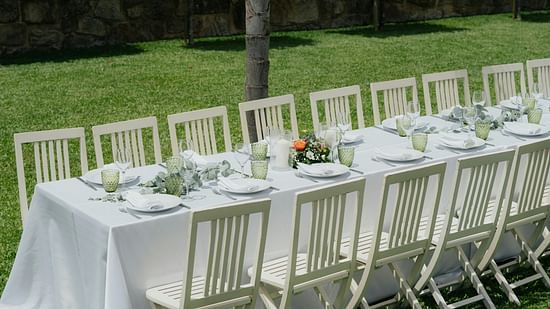 An image of a lawn where chairs and tables are lined up in order with cutlery and floral decoration