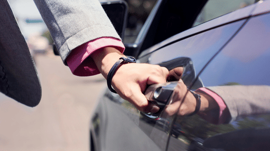 A person holding a car door handle, with part of the vehicle and road visible in the background.