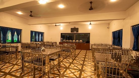 A restaurant with dining tables and chairs arranged with bright lighting and blue curtains - VITS Select Diamond Resort, Sasan Gir
