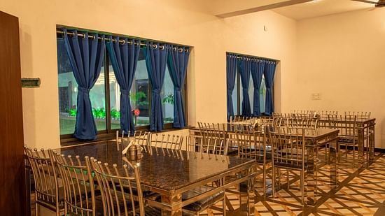 A close up image of the restaurant featuring large windows with blue curtains and neatly arranged chairs with tables - VITS Select Diamond Resort, Sasan Gir