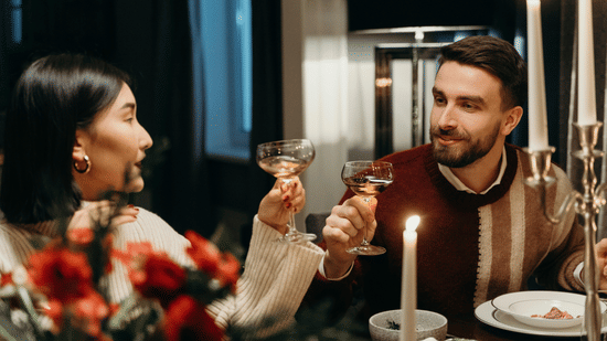 A couple enjoys a candlelit dinner, sharing a toast with glasses of wine in a warm setting.