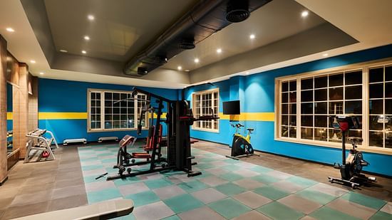 Modern hotel gym with vibrant blue and yellow walls, equipped with strength machines, free weights, and stationary bikes - Voyage The Solitaire Bliss.
