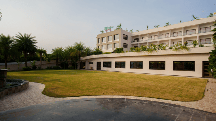 Exterior view of the low-rise hotel building adjacent to a large, well-maintained green lawn area at Arawali Ananta Elite, Jaipur.