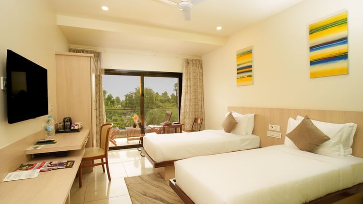 Hotel room with three beds, a television, and brightly coloured artwork at Arawali Ananta Elite, Jaipur.