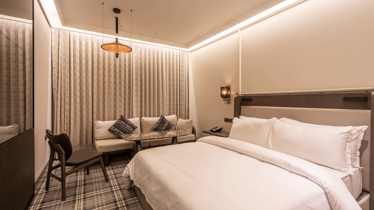 Modern hotel room at The Residency Towers Chennai featuring a large bed, seating area with sofa and chair, patterned carpet, and warm ambient lighting.