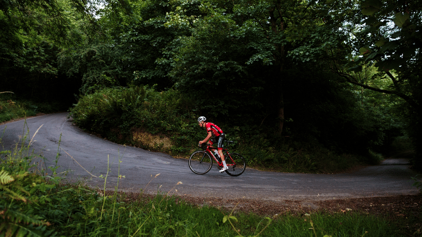 A person is cycling on a path in a green forest.
