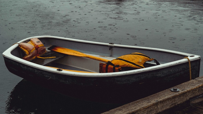 A close of a single seating boat with an oar and a life jacket inside it.