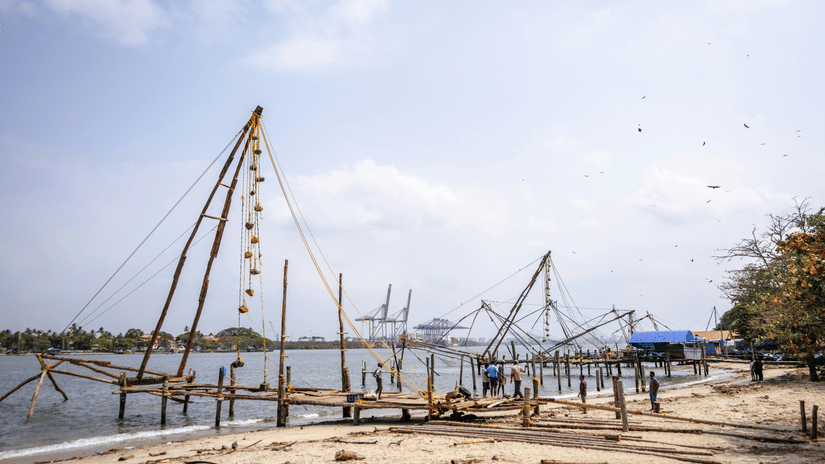 Traditional Chinese fishing nets, Fort Kochi, lining the sandy waterfront under a bright blue sky