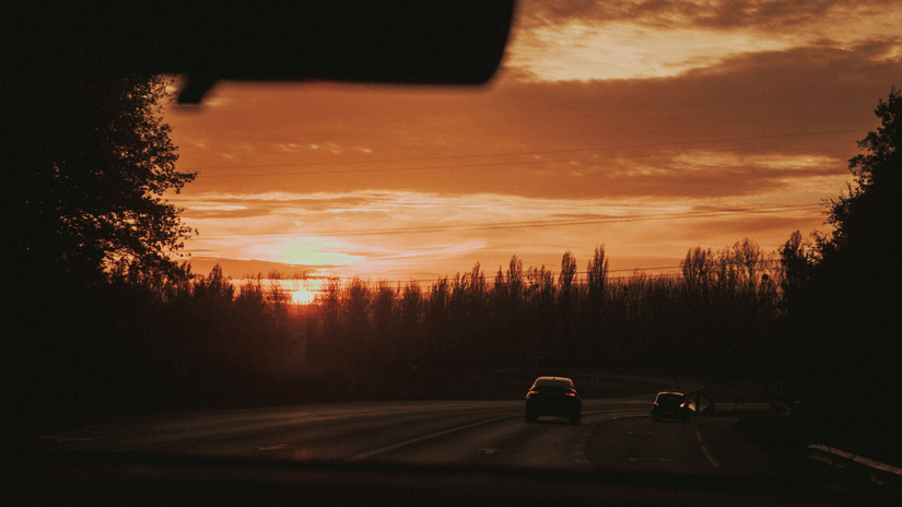 A view of a highway with a solitary car on it and trees all around with the sun setting in the background on the from Coimbatore to Wayanad.