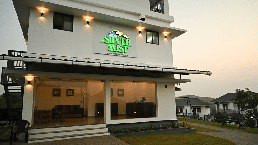 A white multi-storey building with a green resort sign above a glass-fronted entrance area at dusk | Abad Silvermist, Vagamon