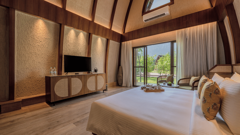 An image of attic style bedroom with a king size bed, a flat TV screen, and a large window from where the outdoor scenes can be enjoyed - Ananta Spa and Resort, Ajabgarh