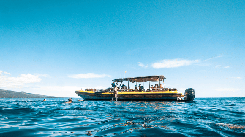 A yellow motorboat floats on calm, deep blue water under a clear sky during a bright, sunny day.