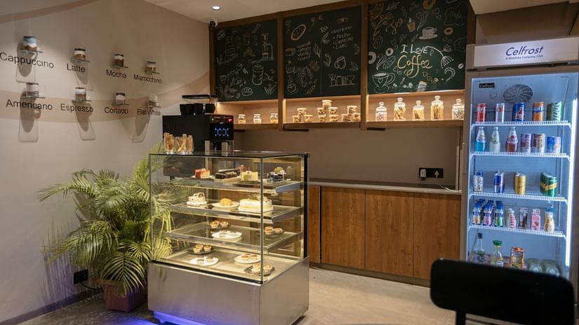 A well-stocked cafe counter with display cases of pastries and beverages, ready for service - Biznotel By Pride Surat