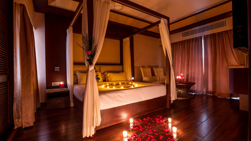 A four-poster bed in a dimly lit room, surrounded by rose petals and candles for a romantic atmosphere - Black Thunder, Coimbatore, one of the best Coimbatore Places to Stay