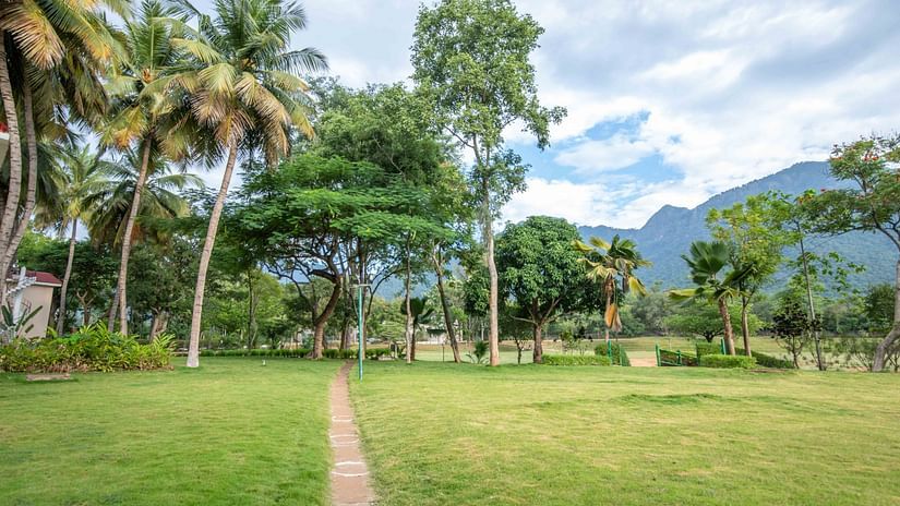 Lush lawn with coconut trees and a distant view of a resort building, set against a backdrop of blue sky and clouds - Black Thunder, Coimbatore