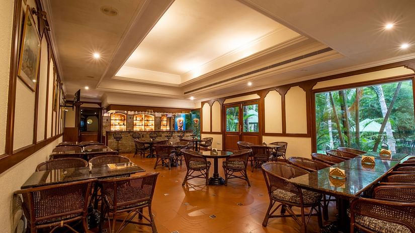 An indoor seating area of a restaurant with wicker chairs and tables, warmly lit with large windows offering a view outside - Black Thunder, Coimbatore