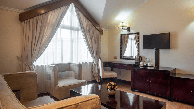 Living room of Suite at Boma Inn Nairobi featuring a sofa set placed in L shape by the window with a coffee table and one facing the TV on the wall next to a mirror