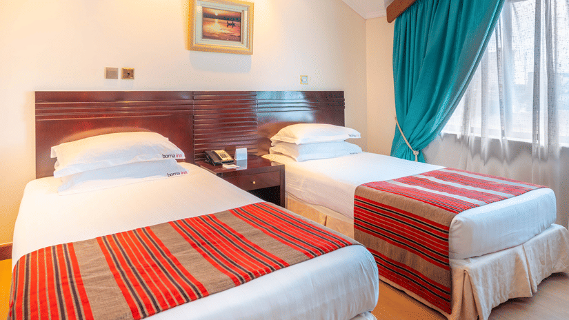 Standard Twin Room featuring twin beds placed next to each other by the window with a common nightstand in the middle at Boma Inn Nairobi