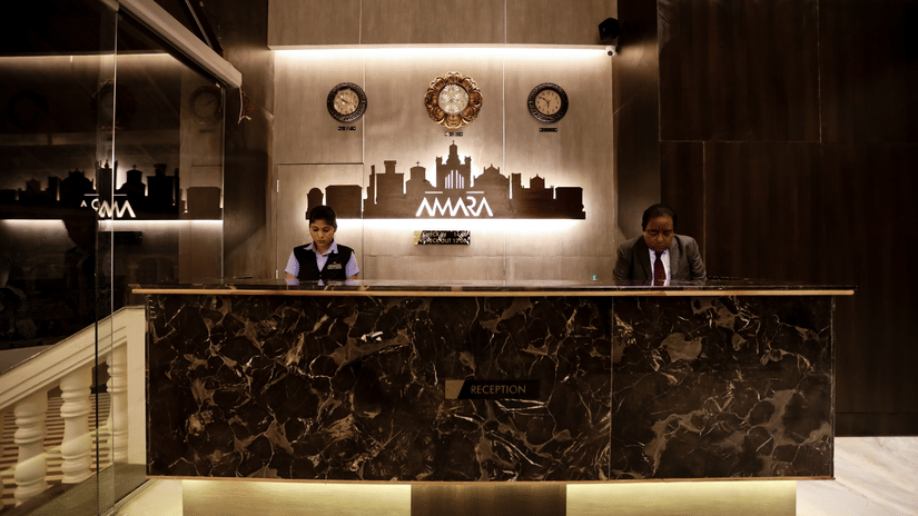 Reception area with a man and a woman standing behind the table at Amara Grand Baga, Goa.