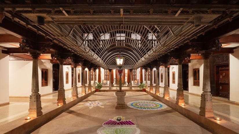 The interior of Chidambara Vilas Resort showing a spacious, traditional Indian assembly hall with ornate wooden architecture and stained glass.