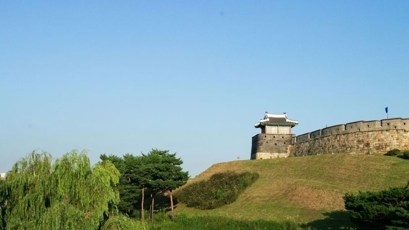 A view from afar of a fort on a hilltop with trees in the foreground and blue sky in the background.