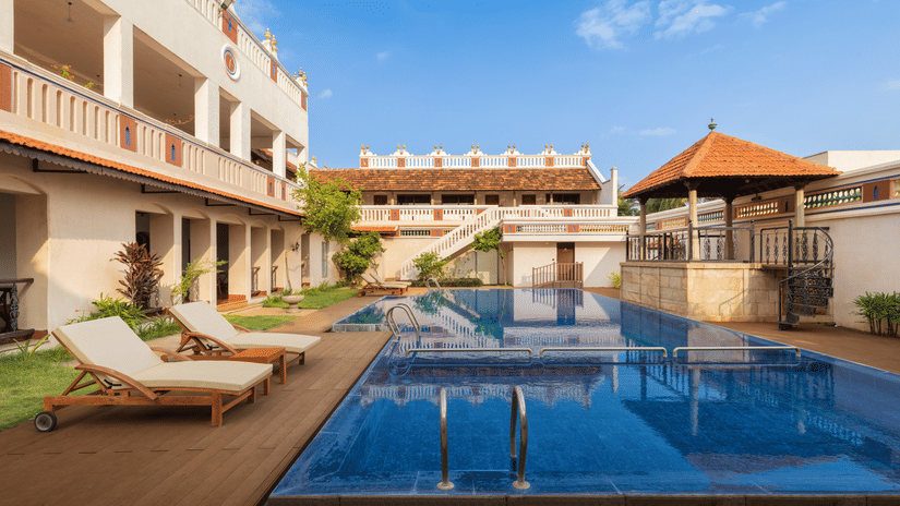 An outdoor swimming pool at Chidambara Vilas Chettinad surrounded by heritage-style architecture with lounge chairs and a shaded pavilion overlooking the courtyard.