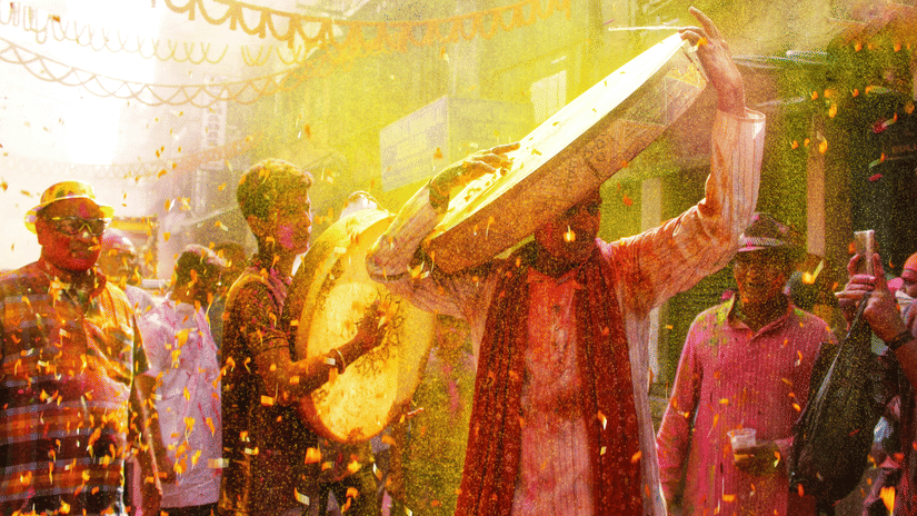 People celebrating a festival, with participants throwing coloured powder and wearing traditional attire.