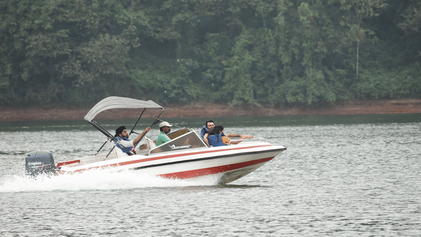 3 people wearing life jackets riding on a speedboat on a lake during daytime.