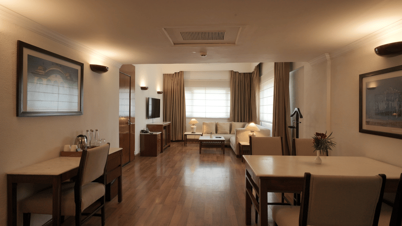 A wide view of the living and dining space with wooden flooring, elegant furniture, wall art, and ambient lighting in the Executive Suite at Clarks Amer, Jaipur.