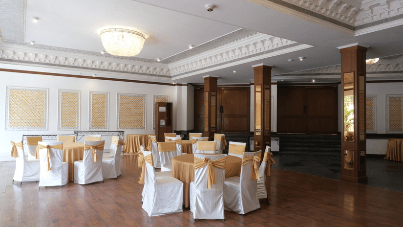 The refined Jal Mahal event venue featuring round dining tables, elegant chair décor, chandeliers, and classic interiors prepared for wedding receptions and family gatherings | Clarks Amer, Jaipur