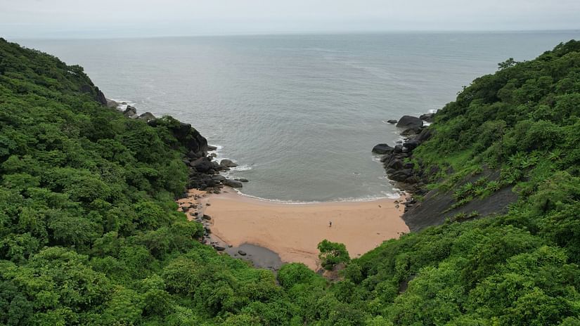 An aerial view of Butterfly Beach in South Goa, surrounded by lush greenery, with the water and sky almost blending seamlessly at the horizon.