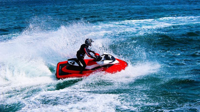 A person in full swimming gear riding a red jet ski in open waters with waves in view.