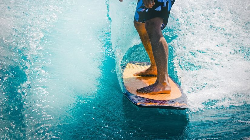A barefoot surfer rides a wave on an orange surfboard in blue ocean waters.