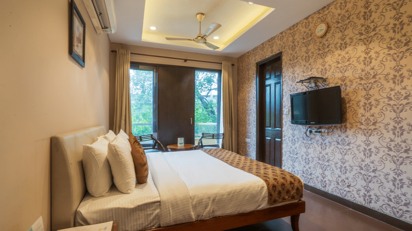 Room at Cosy Grand  at Chanakyapuri by The Cosy Hotels with double bed, balcony view, and flat-screen TV.